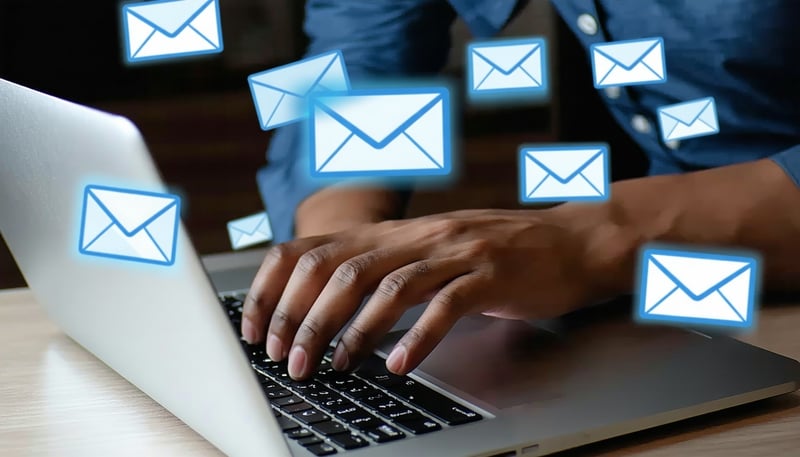 A person typing on a laptop with email icons float