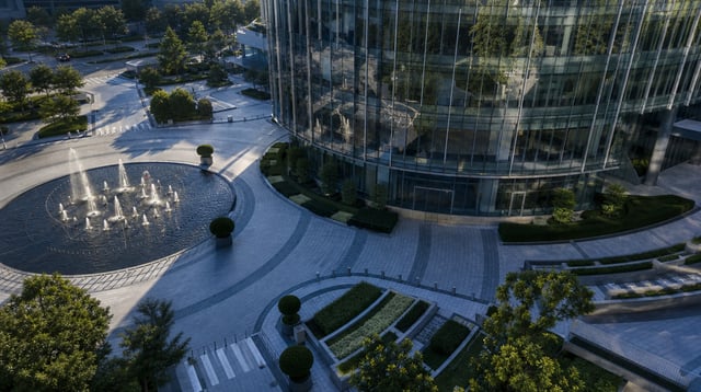 A modern glass office tower plaza with fountains