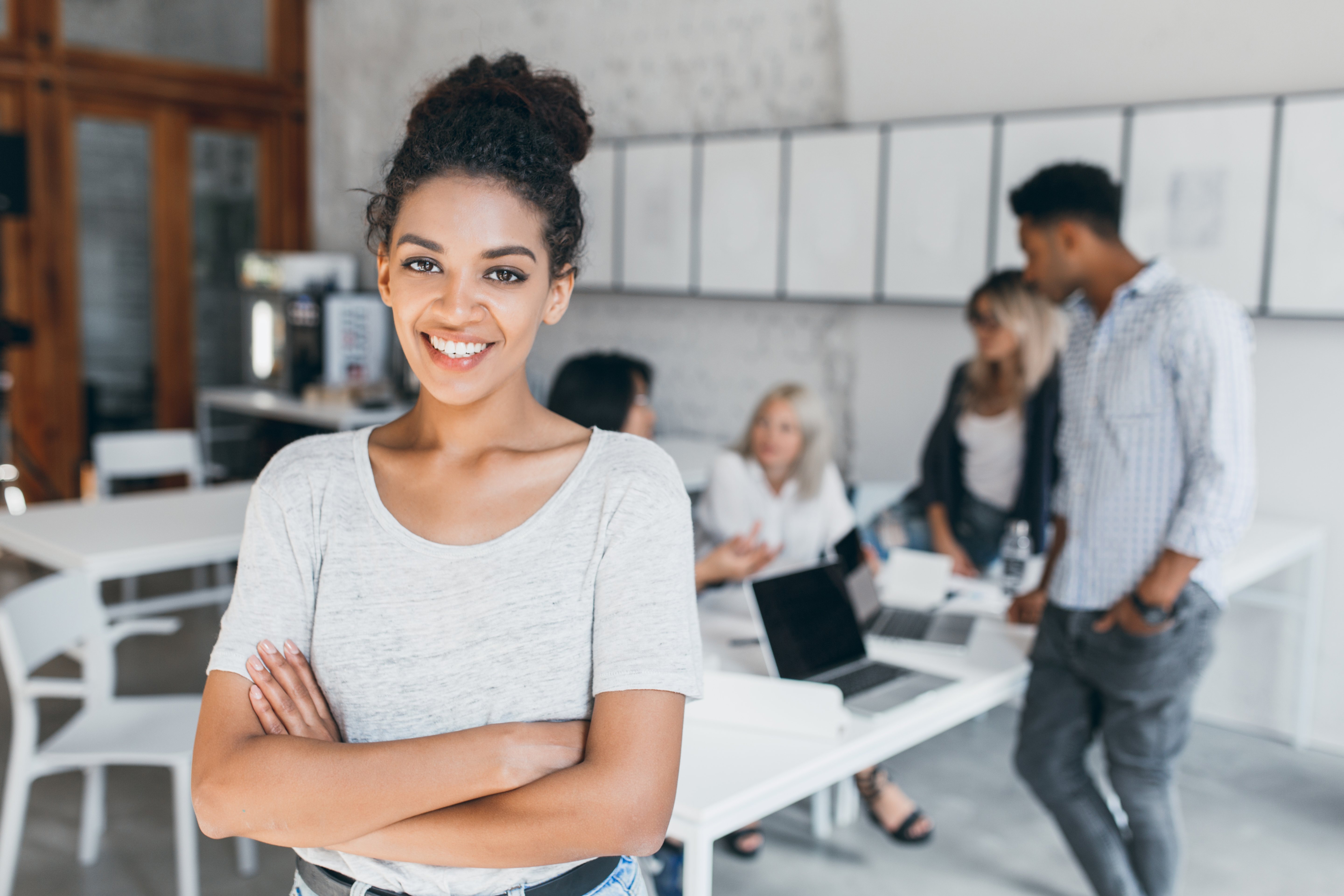 pleased-woman-with-light-brown-skin-posing-with-crossed-arms-smiling-while-people-her-working-indoor-portrait-tired-students-with-laptop-african-curly-girl